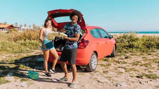 Dos personas sacando una tabla de surf de un coche