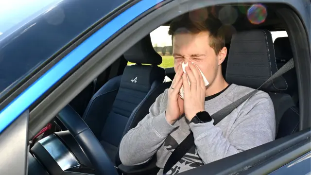 Un hombre sonándose dentro de su vehículo