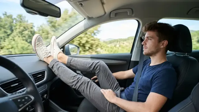 Un pasajero apoya los pies sobre el salpicadero de un coche.